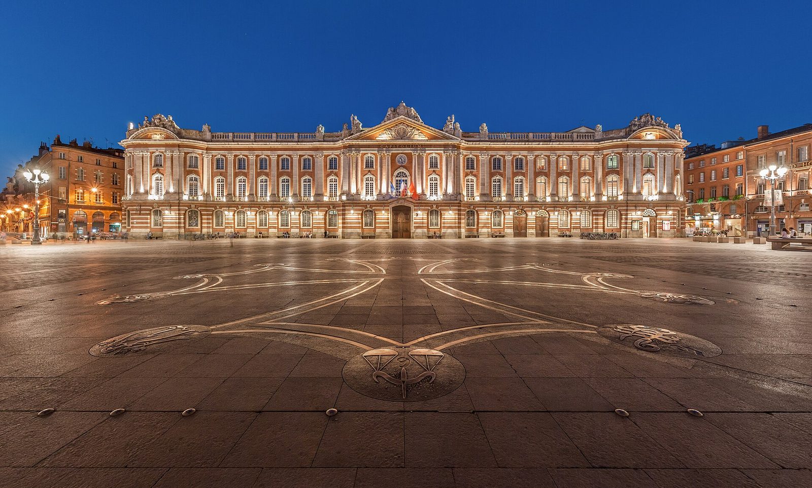 The illuminated façade of Place du Capitole at dusk.