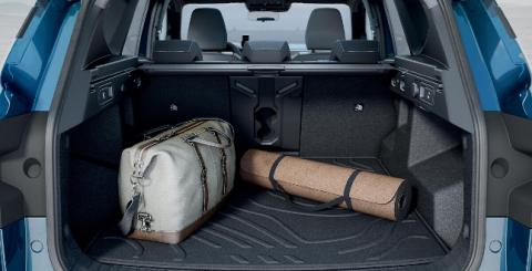 Bagageira aberta de 506 litros do Dacia Bigster carregada com um saco de viagem e um tapete enrolado