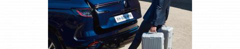 Vue arrière d'un Renault Espace bleu avec un voyageur chargeant des valises dans le coffre (2198 x 450)