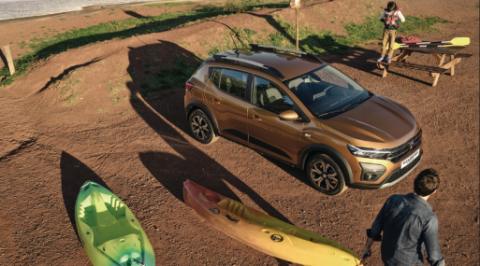 Dacia Sandero Stepway em bronze com barras de tejadilho estacionado junto a um lago, com caiaques descarregados ao lado